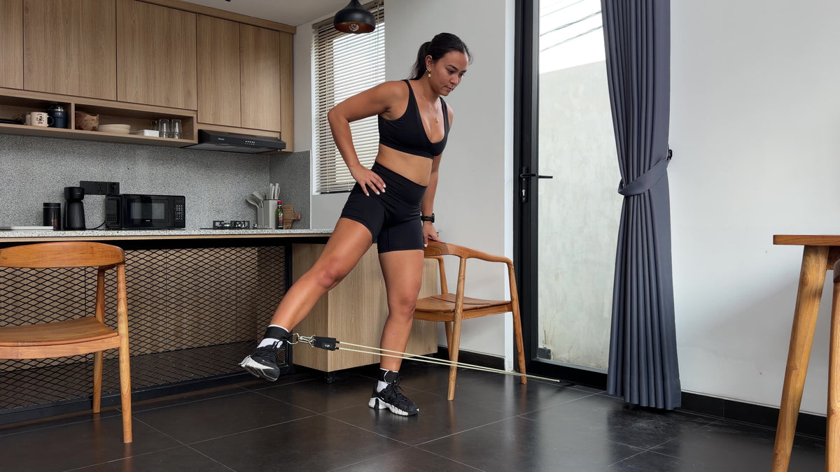 Woman performing a standing lateral leg raise with resistance band ankle attachment in a home setting, using the AEVO Fit Strength System for glute and hip abductor training.